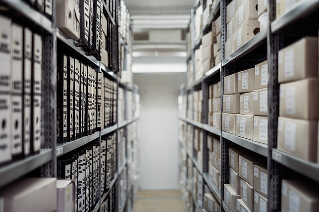 Image shows storage shelves full of boxed-up or bound objects, with full shelves receding into the distance. Image from pixabay.